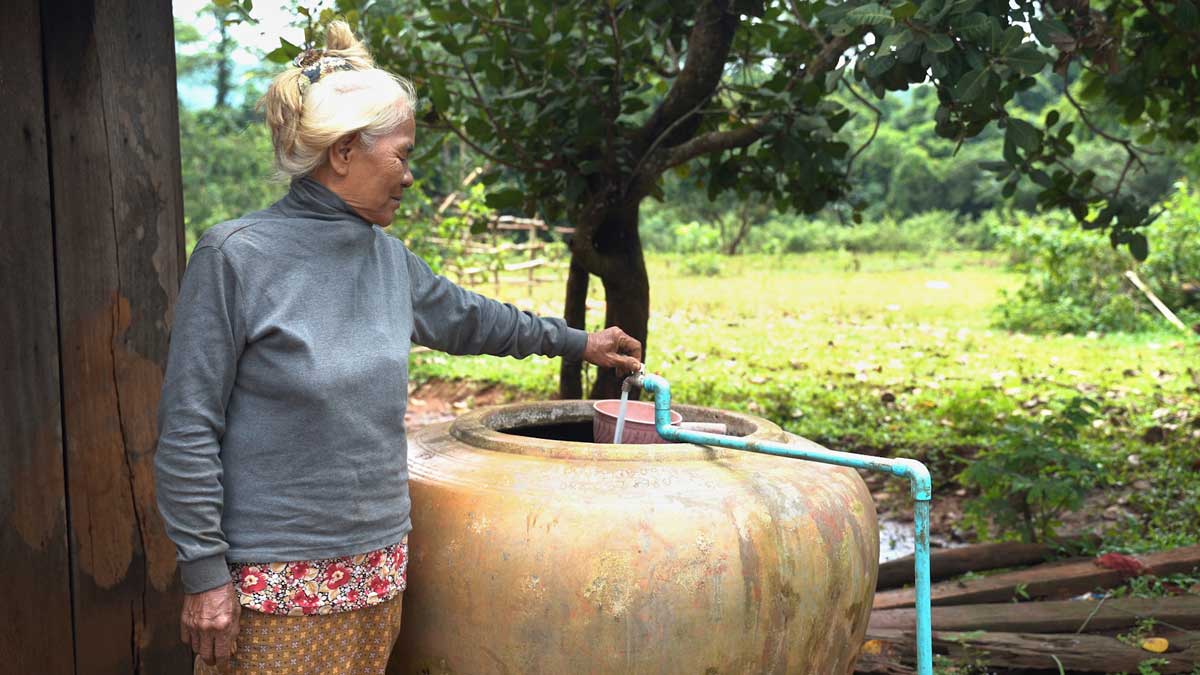 elderly woman standing in front of tapped water tank