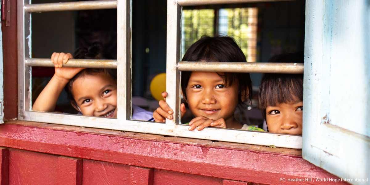 children smiling from inside a classroom in Cambodia