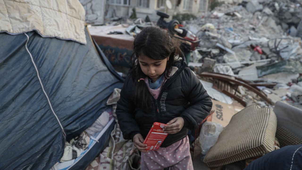 little girl in the middle of rubble next to a tent